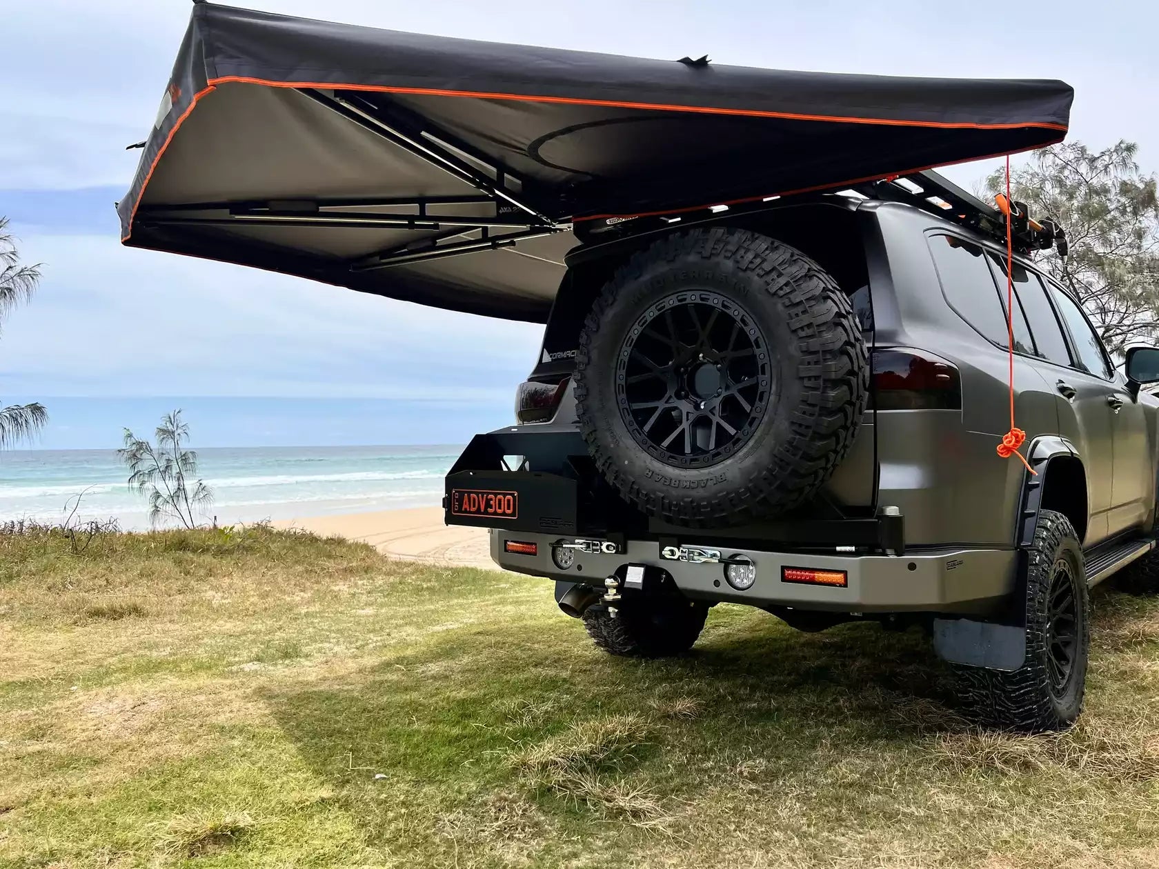 tenda laterale nera Campboss dispiegata su un 4x4 davanti al mare