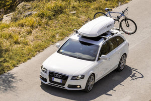 Audi bianca con un box sul tetto bianco e una bicicletta dietro di essa