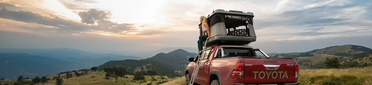 Toyota Hilux rossa equipaggiata con una tenda da tetto James Baroud grand Raid EVO e una donna seduta all'uscita della tenda.