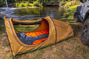 Tenda a terra sull'erba di fronte a un fiume con un piumino arancione all'interno